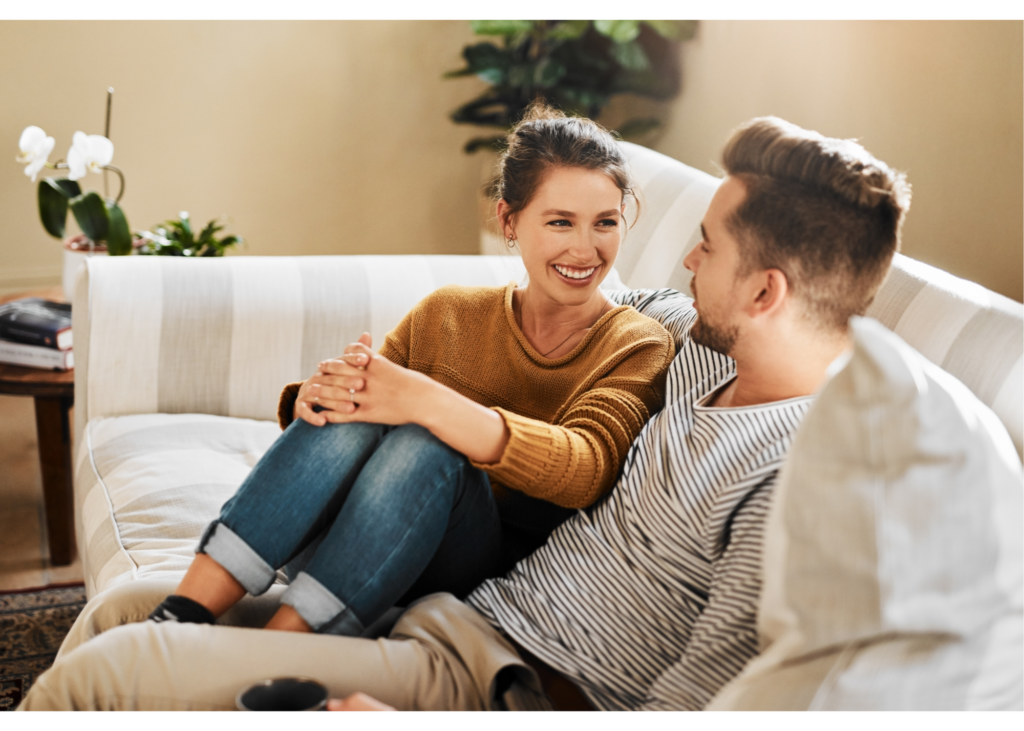 A couple sit and smile at one another on the couch. Learn how therapy for new relationships in New Bern, NC can support a strong foundation. Learn more about life changes counseling in North Carolina and more by contacting an online therapist in North Carolina today.