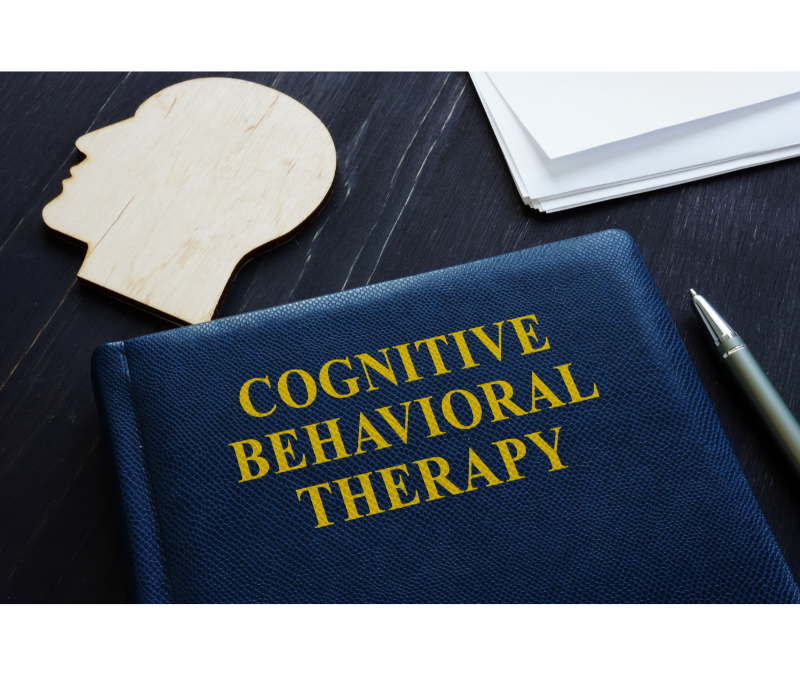 A close-up of a book titled Cognitive Behavioral Therapy on a desk. Learn more about CBT therapy in New Bern, NC, and the support a CBT therapist in North Carolina can offer from the comfort of home. An online therapist in North Carolina can support you today!