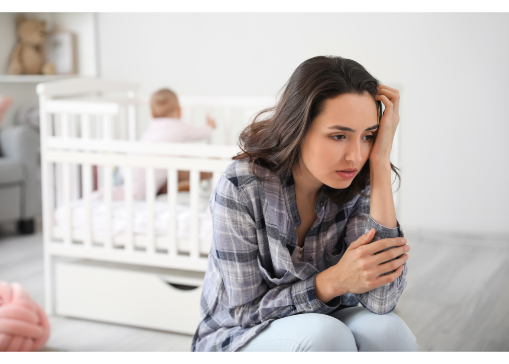 A mother sits facing away from her baby’s crib representing the concerns with postpartum mental health. Learn more about life transitions counseling near me by contacting a life transition therapist in New Bern, NC. 