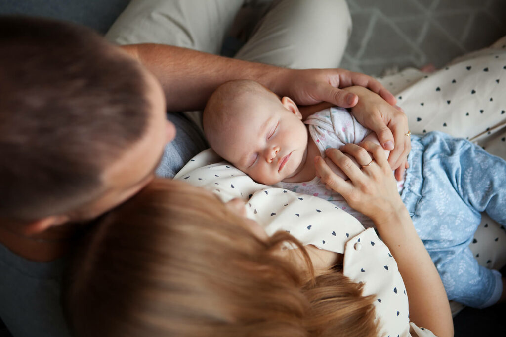 A baby sleeps in the arms of their parents. Contact a life transition therapist in New Bern, NC for support with postpartum mental health. Learn more about life changes counseling in North Carolina today by searching for life transitions counseling near me. 