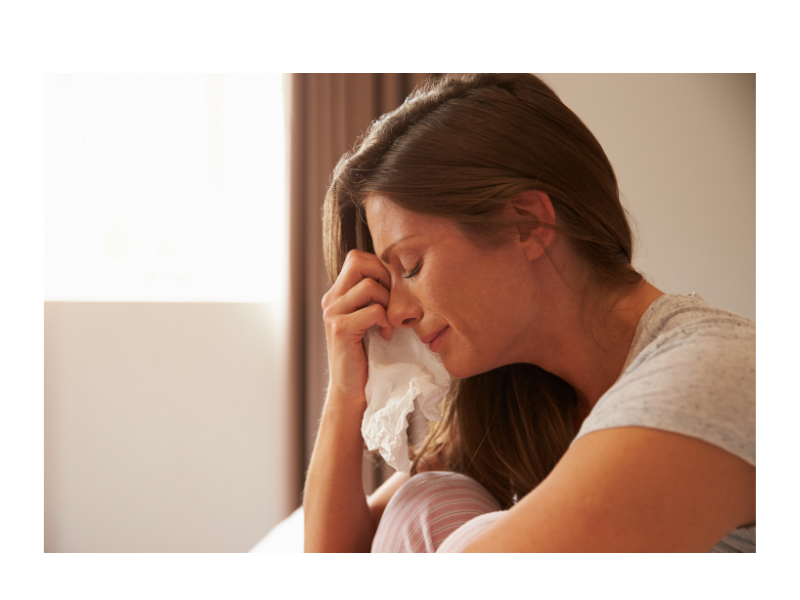 A woman pinches her nose while crying and holding a tissue. This could represent the pain of grief that online trauma therapy in North Carolina can address. Learn more about the support a therapist in New Bern, NC can offer by contacting a trauma therapist in New Bern, NC. Learn more about trauma therapy in New Bern, NC, and other services today. 