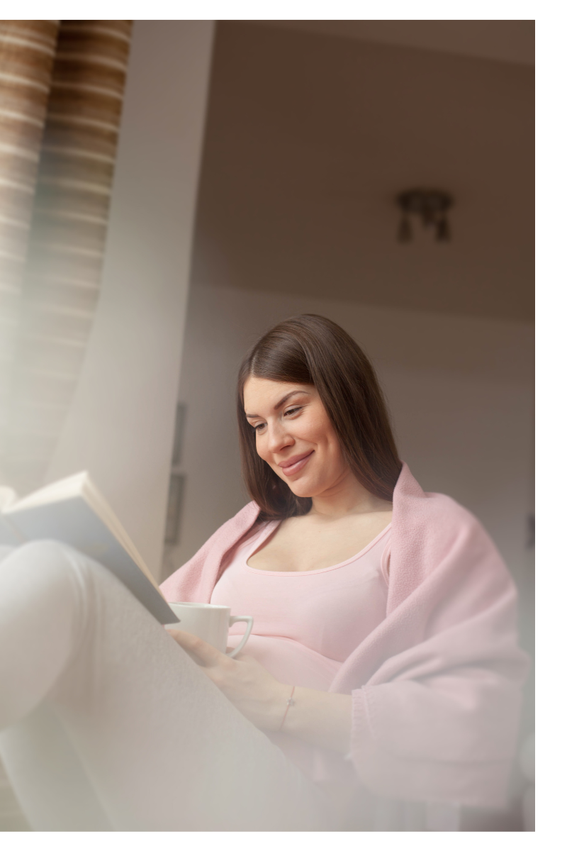 A woman smiles while reading a book and drinking coffee. Learn how a New Bern therapist can offer support with coping with therapy for anxiety in New Bern, NC. Search for anxiety treatment for support with new parents in New Bern, NC. 