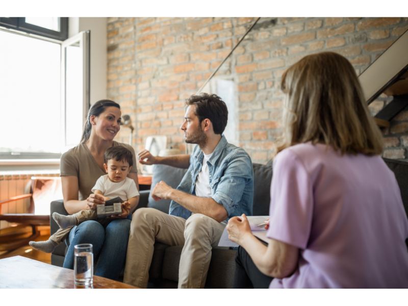 A family of three talk while sitting next to a person with a clipboard. Learn how a New Bern therapist can offer support for new parents in New Bern, NC. They can offer therapy for anxiety in New Bern, NC and other services. 
