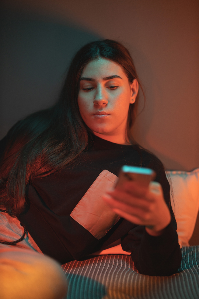 woman laying on bed in dark room looking at mobile phone. Dark side of social media. Online Therapy 28562