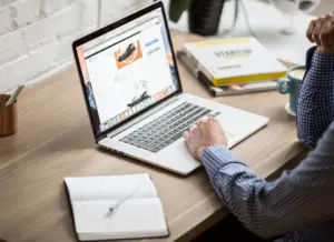 Person browsing a wellness-related website on a laptop at a wooden desk with a notebook and coffee cup nearby
