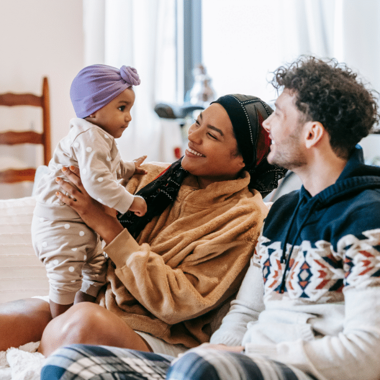 Smiling parents bonding with their baby at home, highlighting emotional connection and support during early parenthood.