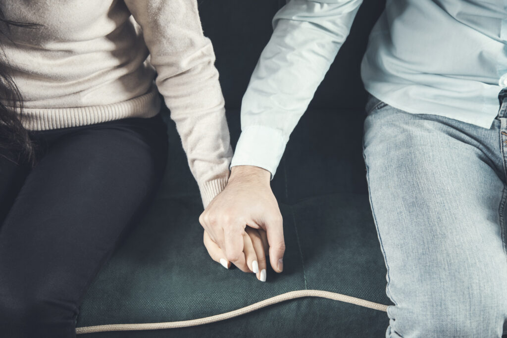 man and woman hold hands sitting on sofa relationship therapy in North Carolina