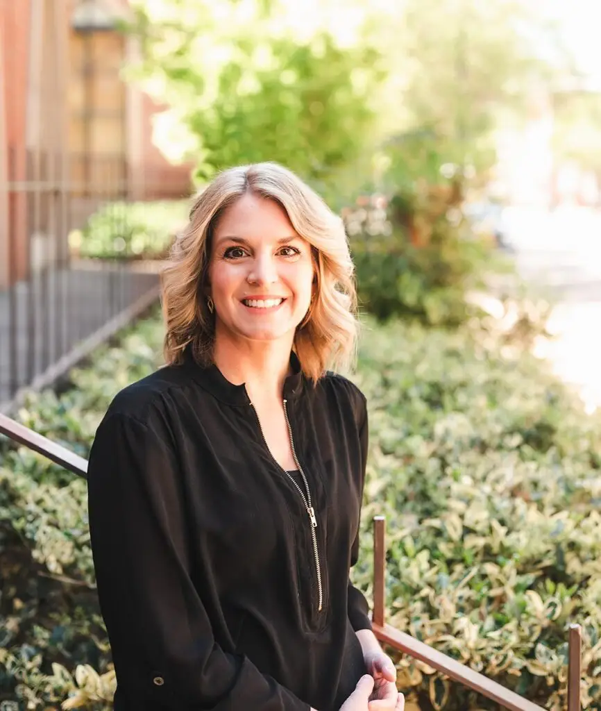 Marcy Arnold, LCSW, LISW-CP, LCAS, smiling outdoors in professional attire, standing in front of greenery and a sunlit walkway