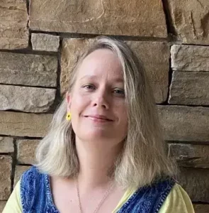 Jessica Williford, LCSWA therapist at Renewed Wellness Counseling, smiling in front of stone wall, wearing yellow top and denim vest.