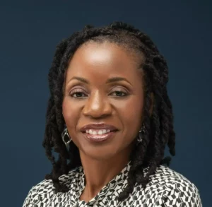 Olayinka Dykes, LCMHC therapist at Renewed Wellness Counseling, smiling confidently in patterned top against dark blue background.