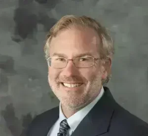 Rob Heubel, LMFT therapist at Renewed Wellness Counseling, smiling in suit and tie, with glasses, studio backdrop.