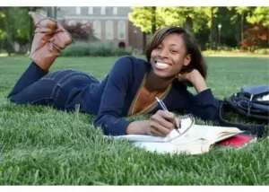 Smiling student journaling on campus lawn – promoting mental wellness and self-care.