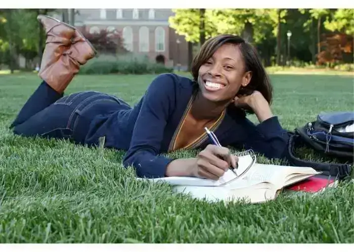 Smiling student journaling on campus lawn – promoting mental wellness and self-care.