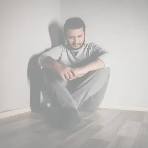 Man sitting alone on the floor in a corner, looking down with a distressed expression — symbolizing anxiety, isolation, and emotional struggle.