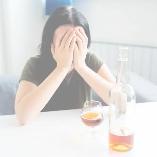 Stressed woman with head in hands at table with alcohol, symbolizing anxiety, emotional distress, and mental health struggle.