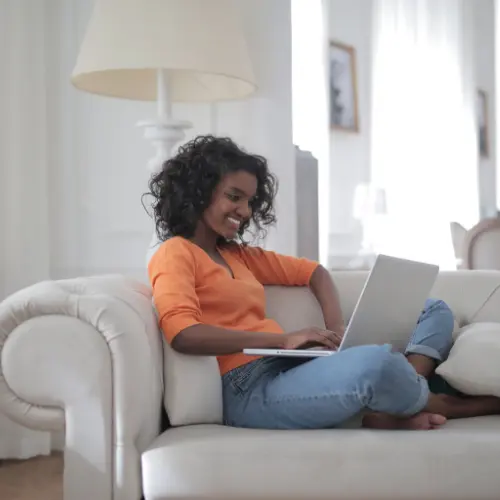 Smiling woman on sofa using laptop, representing online therapy, telehealth, or virtual counseling session.