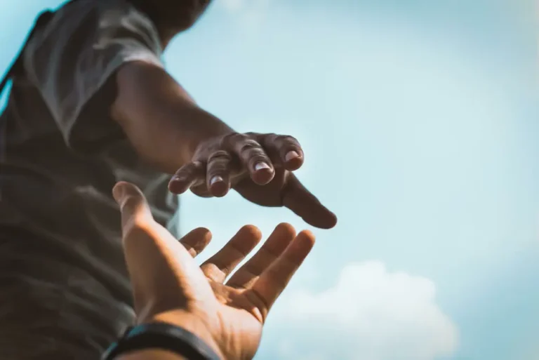 Two hands reaching toward each other against a blue sky, symbolizing help, support, or connection.