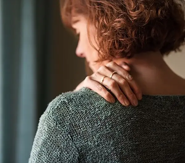 Woman holding her neck and shoulder, possibly experiencing chronic pain or tension.