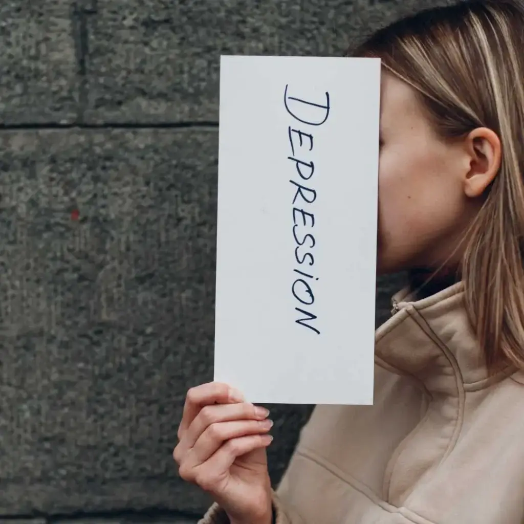 A woman holding a sign labeled “Depression” in front of her face, symbolizing hidden emotional struggles.