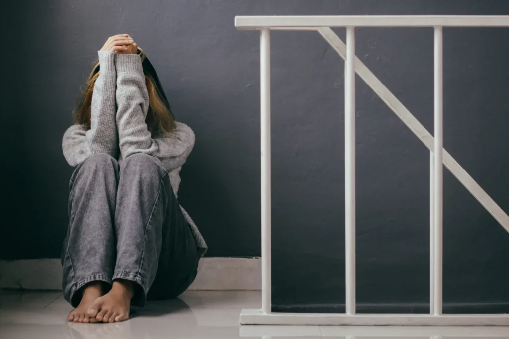 A woman sits on the floor with her head in her hands, conveying deep sadness and emotional distress.