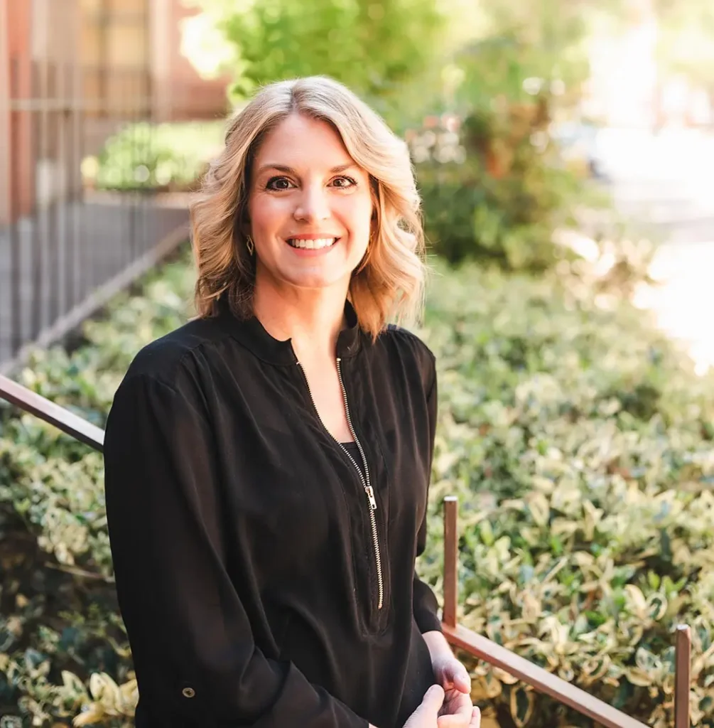 Marcy Arnold, LCSW, LISW-CP, LCAS, smiling outdoors in professional attire, standing in front of greenery and a sunlit walkway