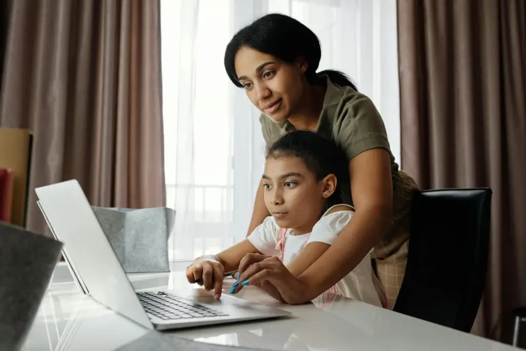 Mother supporting daughter as she works on a laptop at home.