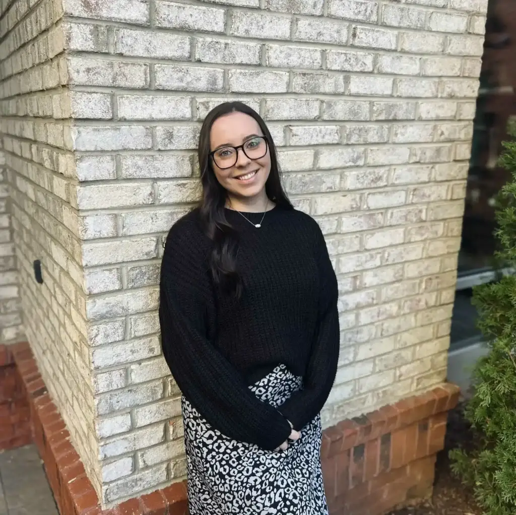 Savannah Reed, LCSW therapist in North Carolina, smiling and standing against a light brick wall in professional attire.