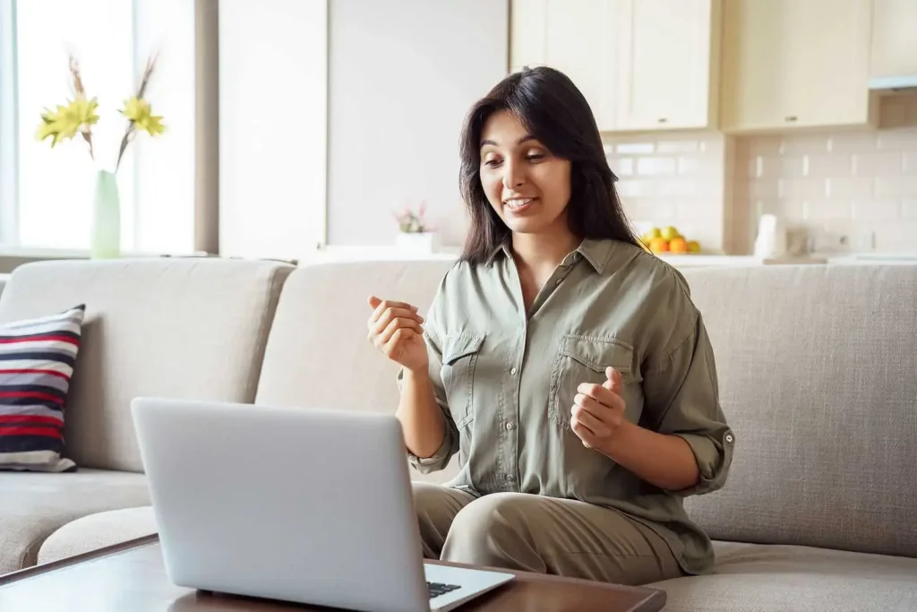 Woman speaking with therapist during virtual counseling session from home using laptop on living room couch.