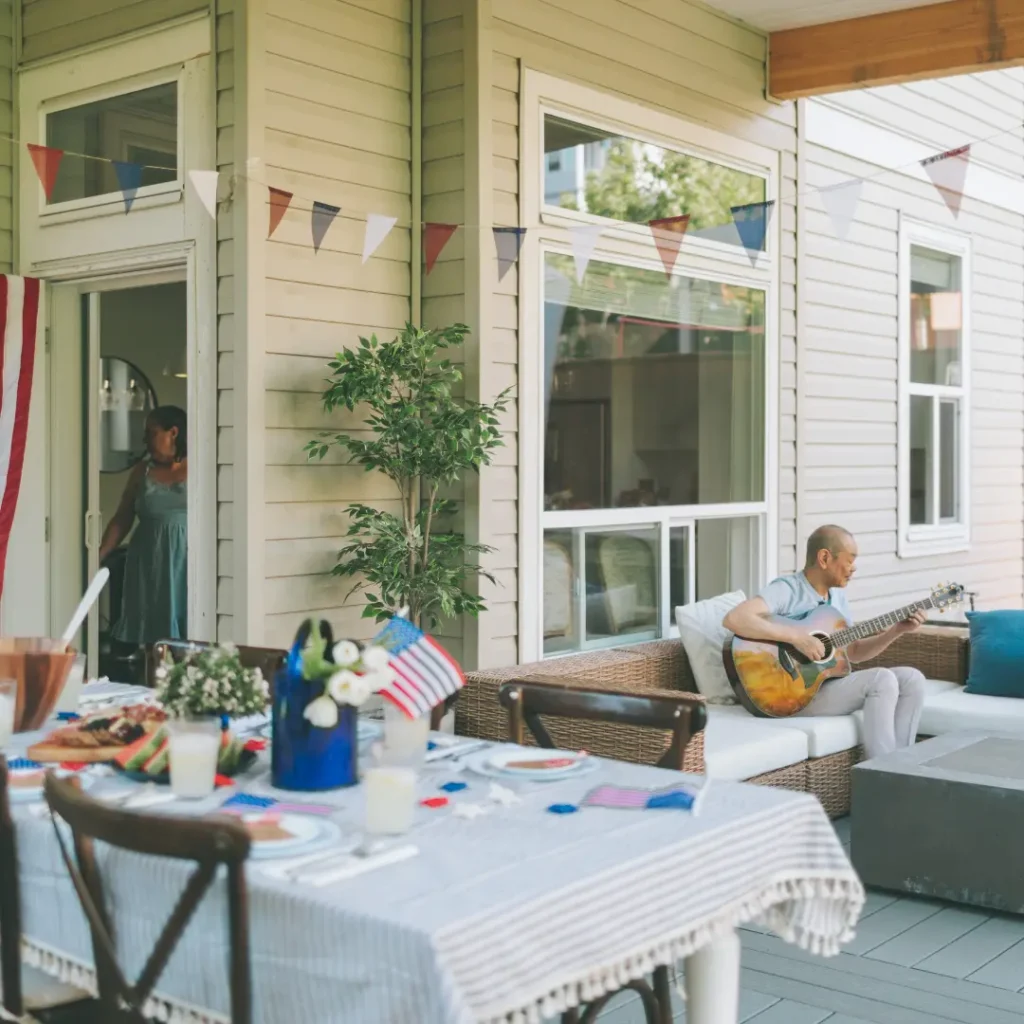 Outdoor summer gathering with patriotic decorations; man playing guitar on the patio while a woman prepares inside — balancing social connection and self-care during chronic illness, Renewed Wellness Counseling, New Bern NC