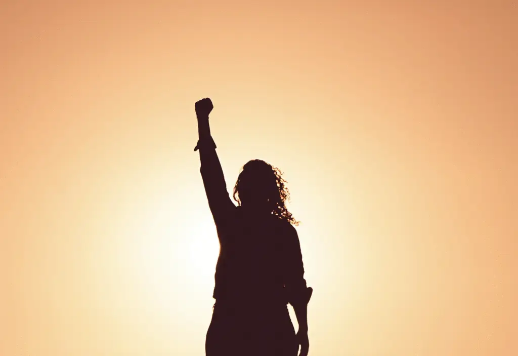 Silhouette of a person raising a fist in the air at sunrise, symbolizing hope, strength, and recovering from depression.
