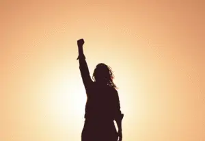 Silhouette of a person raising a fist in the air at sunrise, symbolizing hope, strength, and recovering from depression.