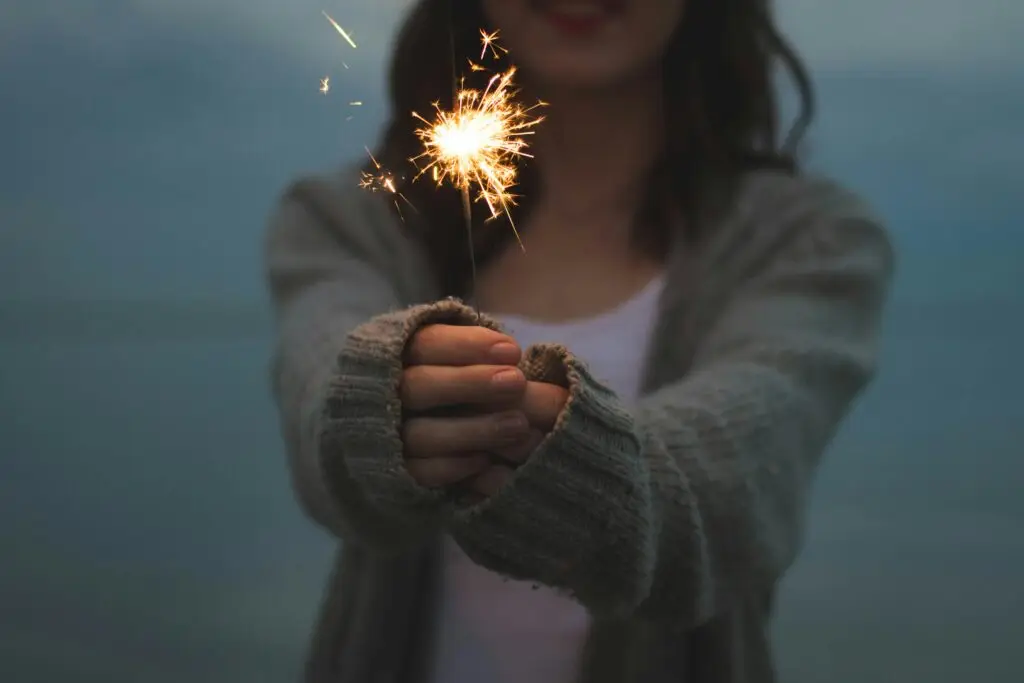 Woman holding a lit sparkler with a gentle smile, symbolizing hope, renewal, and finding joy after depression.