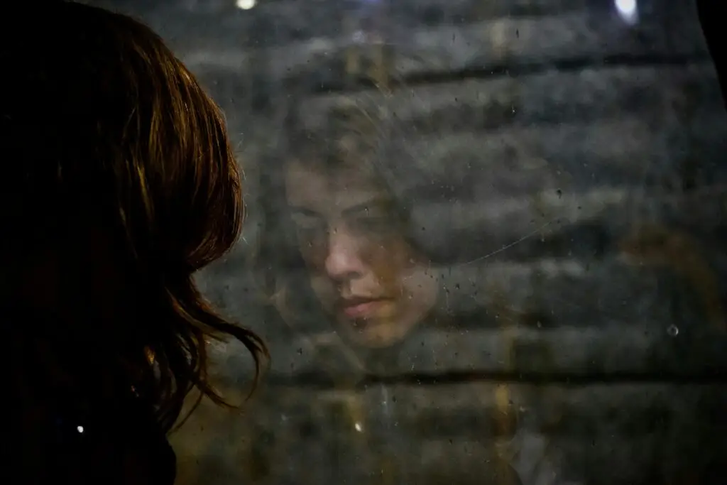 Woman looking down with her reflection visible in a window, illustrating the heaviness and inward struggle often experienced with depression.