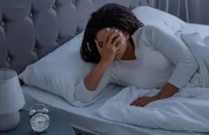 Woman lying awake in bed with her hand on her face, illustrating the frustration of insomnia addressed through CBT-I therapy.