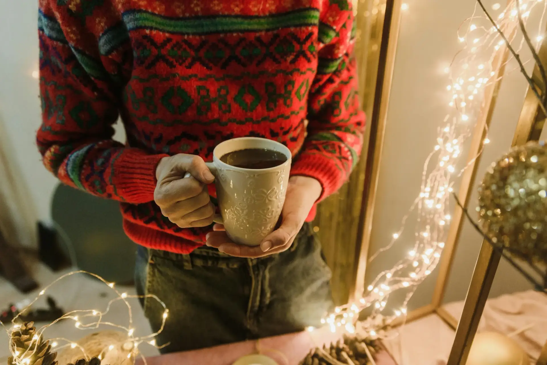 Person holding a warm mug near holiday lights as a grounding moment, representing coping tools from online therapy in NC SC VA