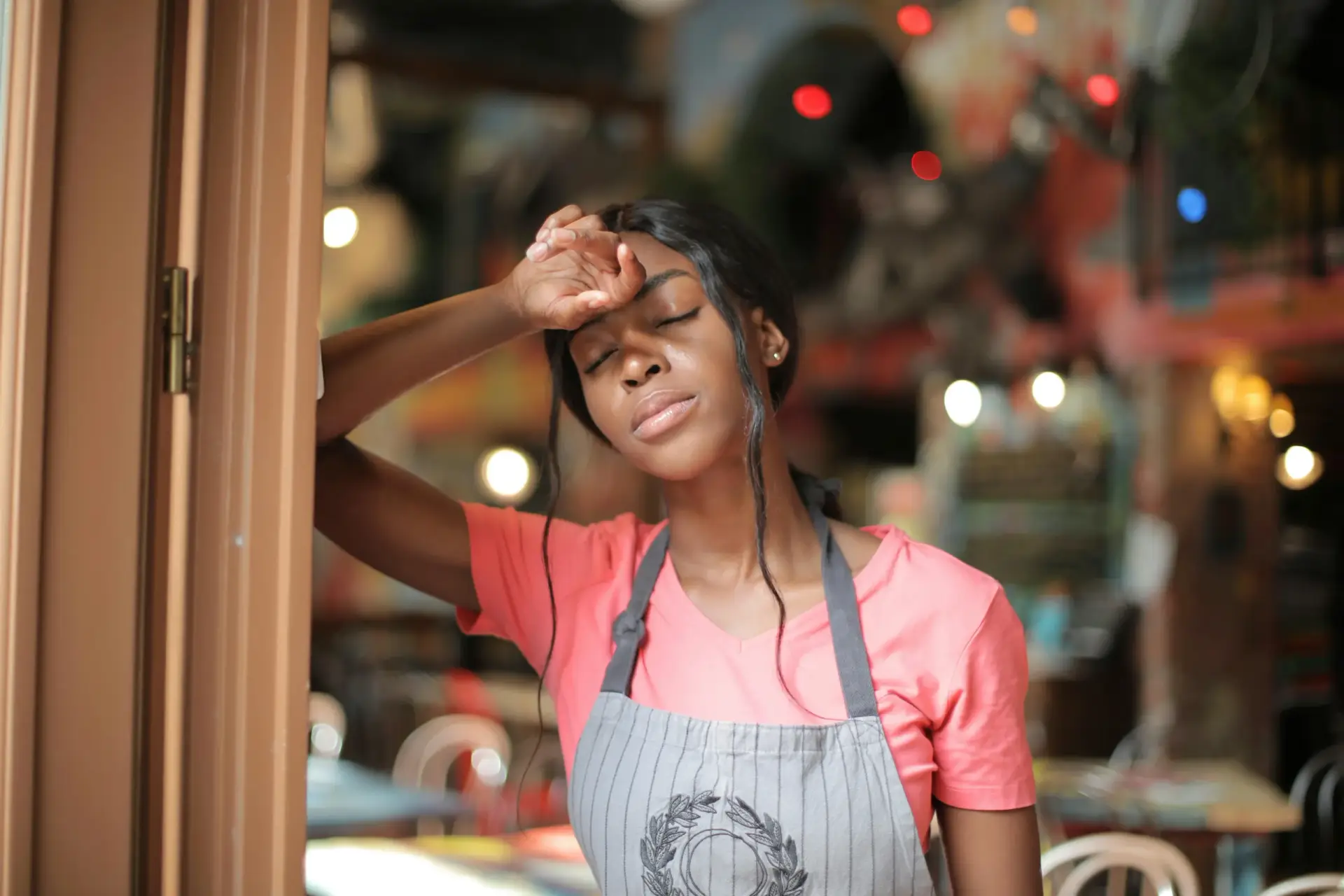 Woman in an apron leaning against a doorway, feeling overwhelmed during the holidays.