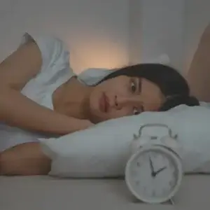 Woman lying awake in bed at night with a clock nearby, showing insomnia before starting CBT-I therapy.