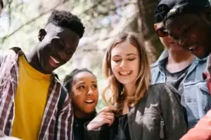 Group of young adults smiling together outdoors, supporting each other and enjoying time outside.