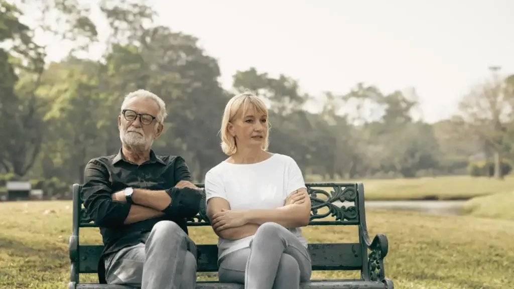 Couple sitting on a bench with arms crossed, showing emotional distance and disconnection often seen in relationships affected by trauma
