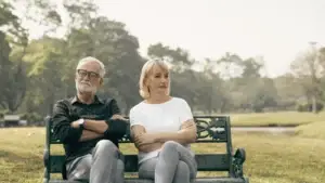 Couple sitting on a bench with arms crossed, showing emotional distance and disconnection often seen in relationships affected by trauma