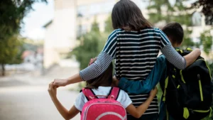 Mom with two school-aged children carrying backpacks during the back-to-school transition