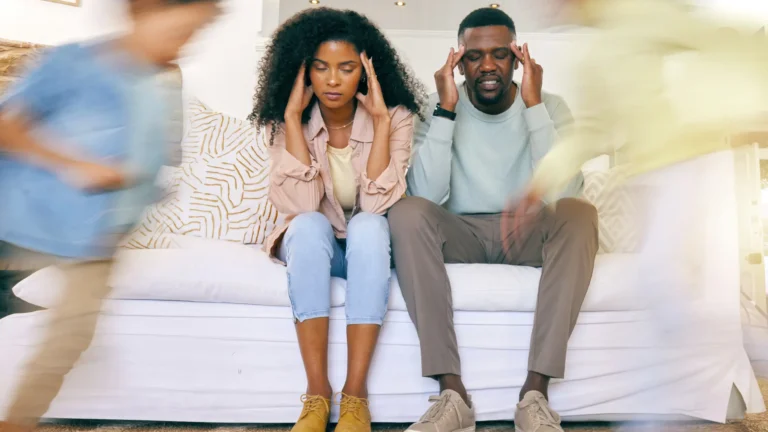 Overwhelmed parents sitting on a couch while their children rush around them