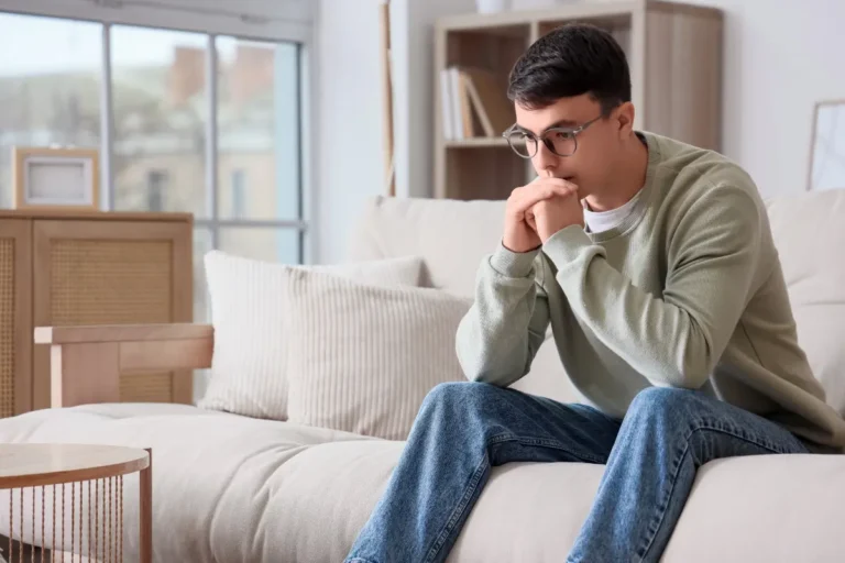 Man sitting on a couch with his hands clasped near his face