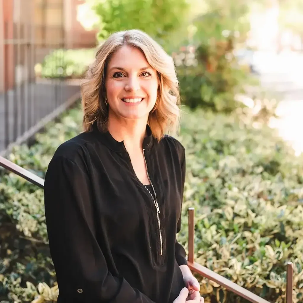 Marcy Arnold, LCSW, LISW-CP, LCAS, smiling outdoors in professional attire, standing in front of greenery and a sunlit walkway