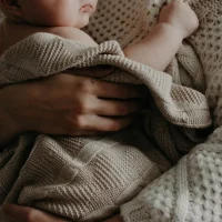 Mother holding her newborn close in a soft blanket, representing the emotional challenges and support needs of postpartum mental health.
