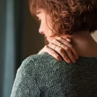 Woman holding her neck and shoulder, possibly experiencing chronic pain or tension.