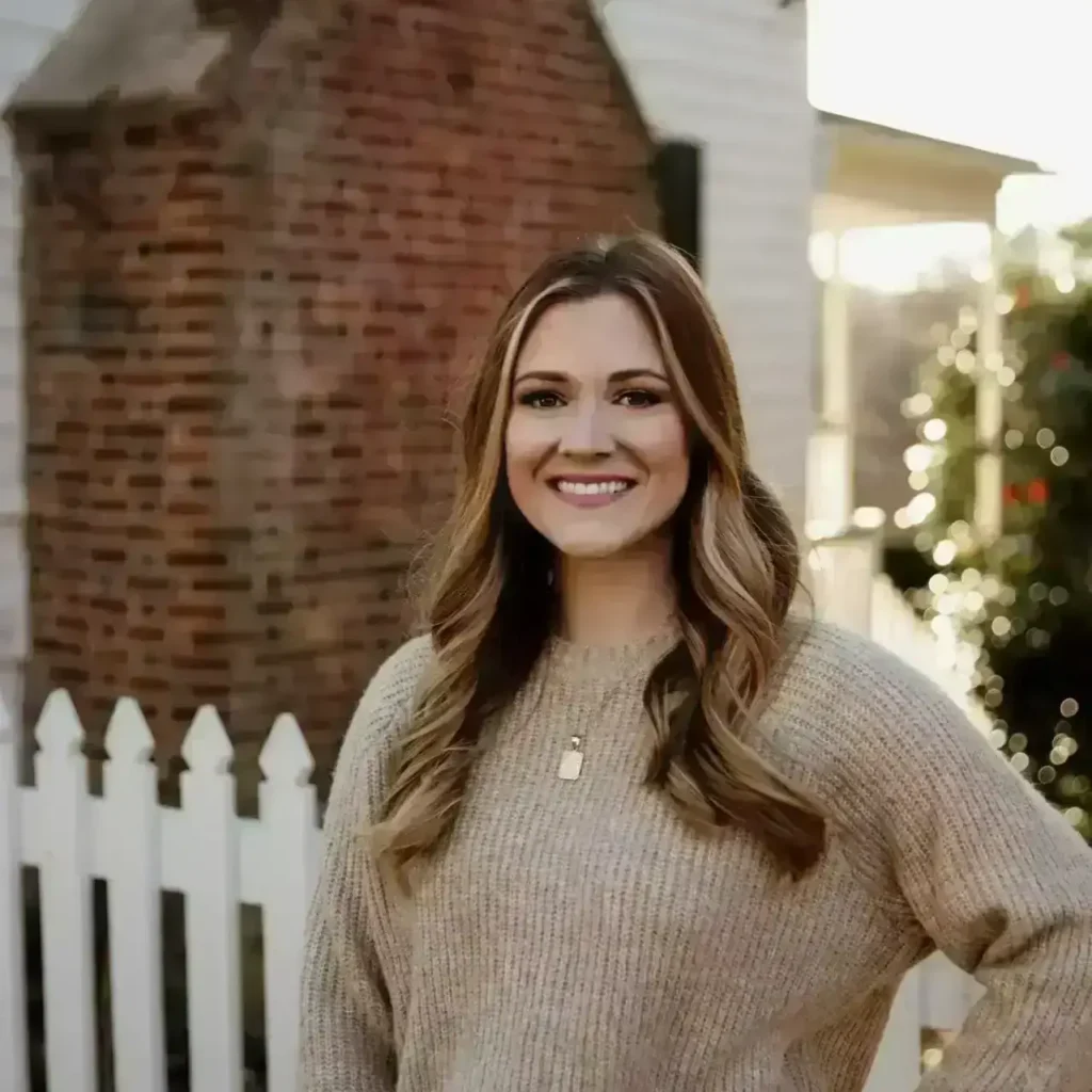 Kaitlyn Moore, LCSW at Renewed Wellness Counseling, smiling outdoors in a sweater, standing by a white fence.